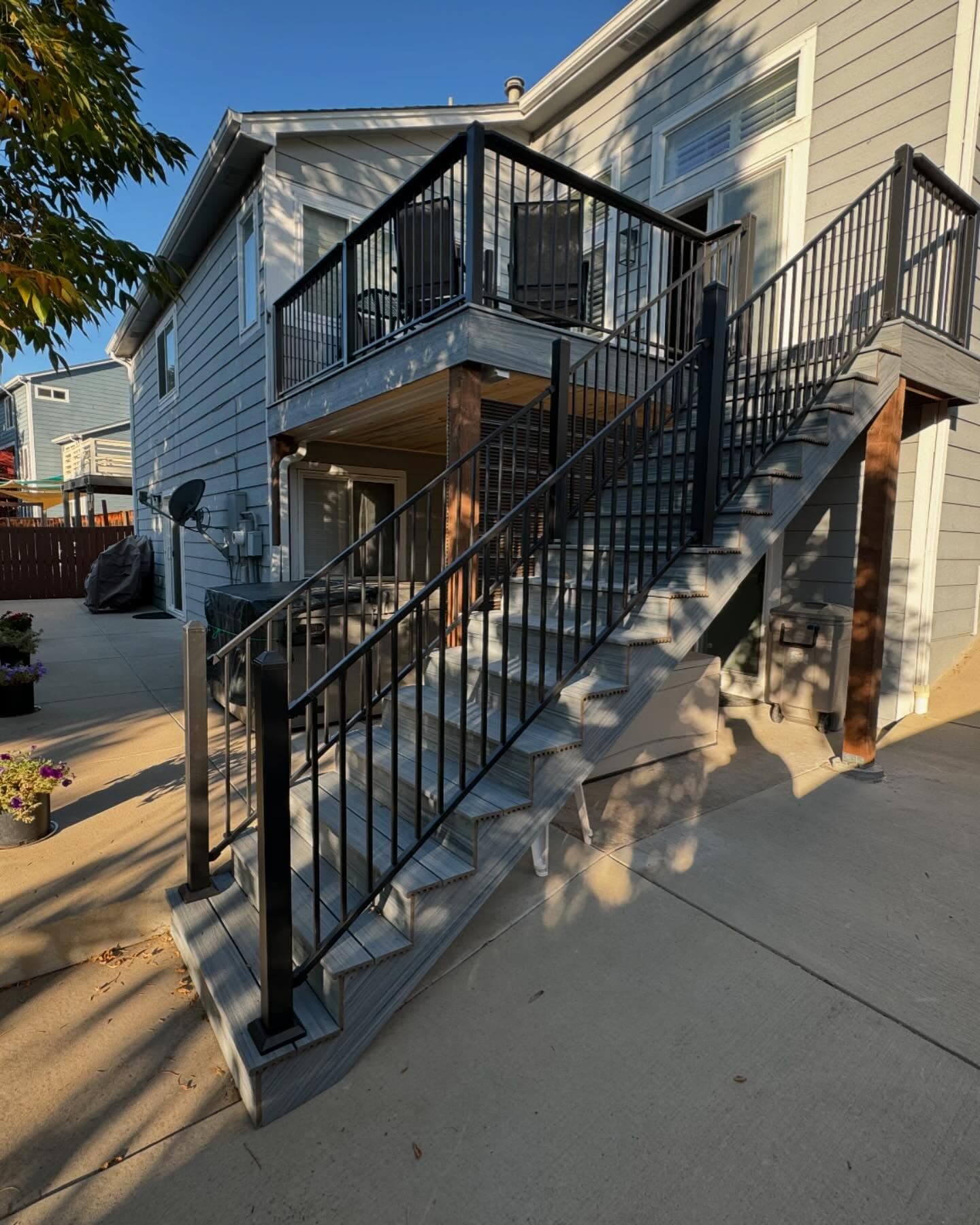 Gray composite deck and matching stair run with black aluminum railing off the back of a two-story home