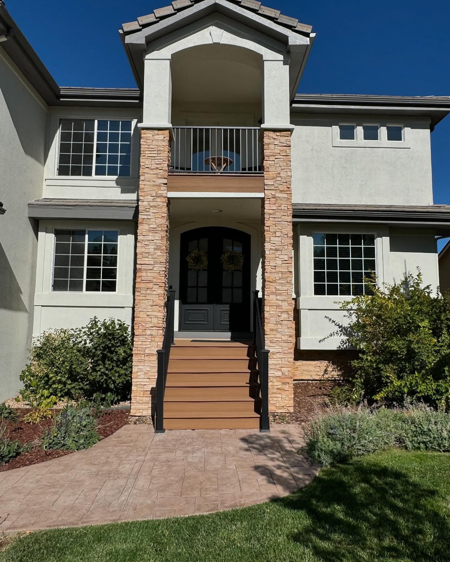 Composite front entry stairs with black railing between stone columns on a stucco home