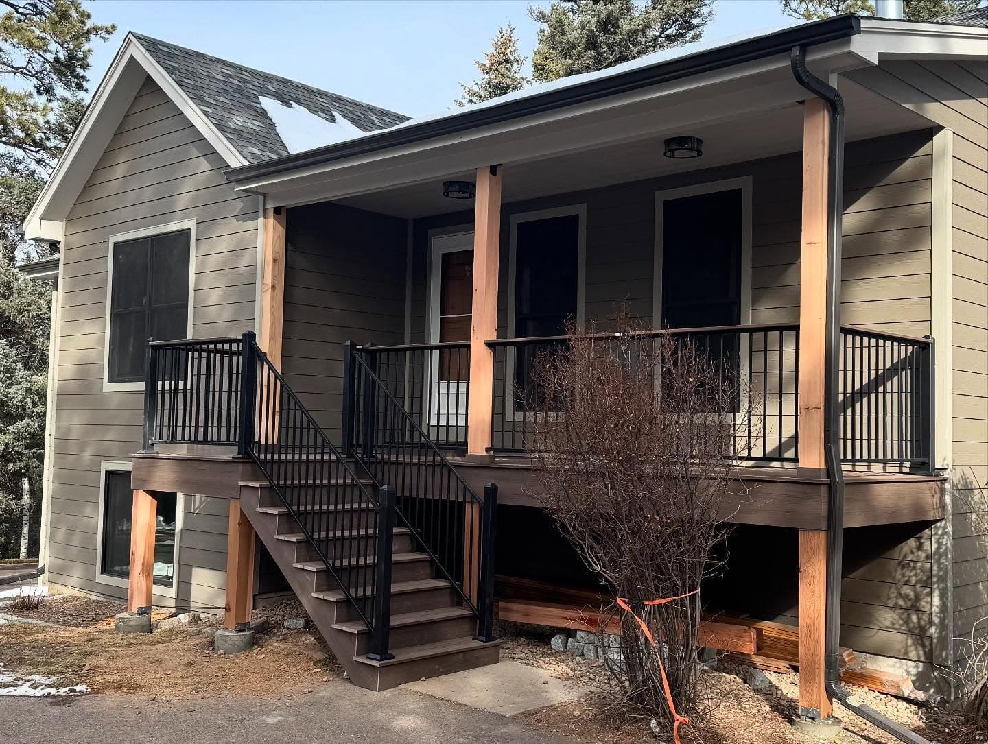 Covered front porch deck with cedar posts, black railing, and stairs on a mountain-style home