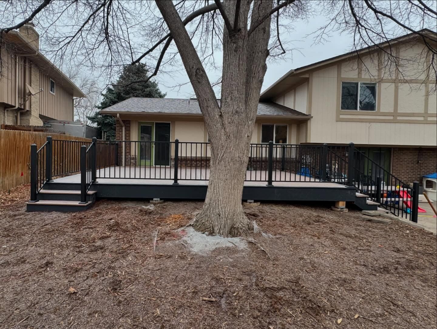 Ground-level composite deck built around a mature tree with black aluminum railing