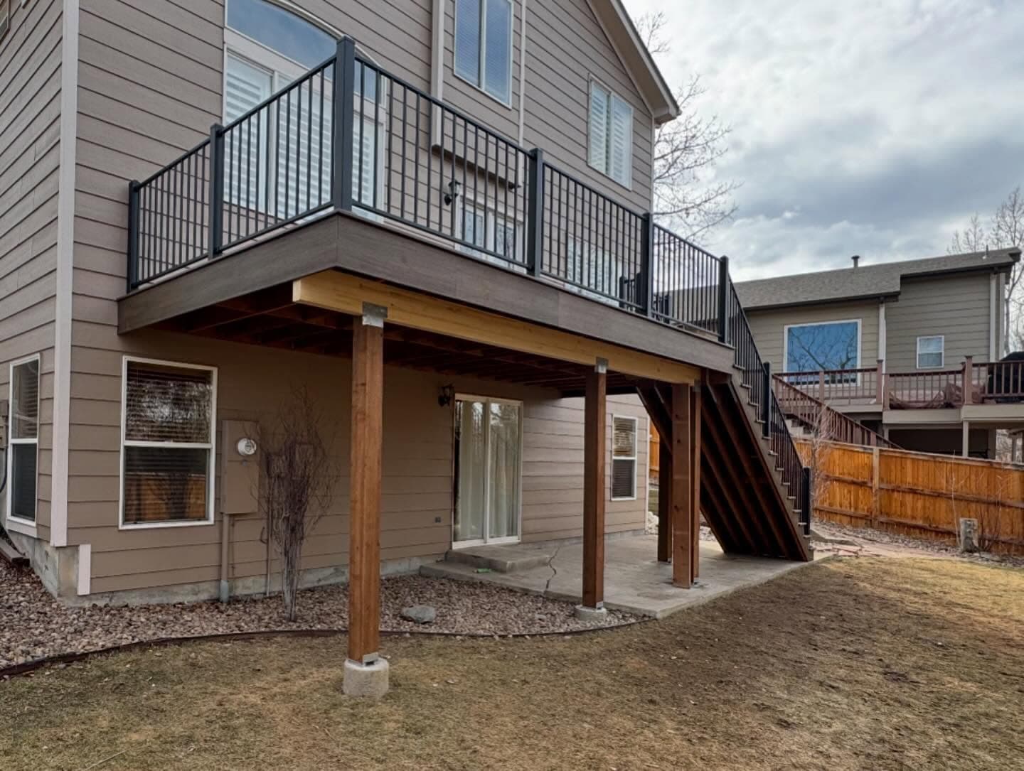 Raised deck on cedar posts with black railing and stairs, over a covered concrete patio