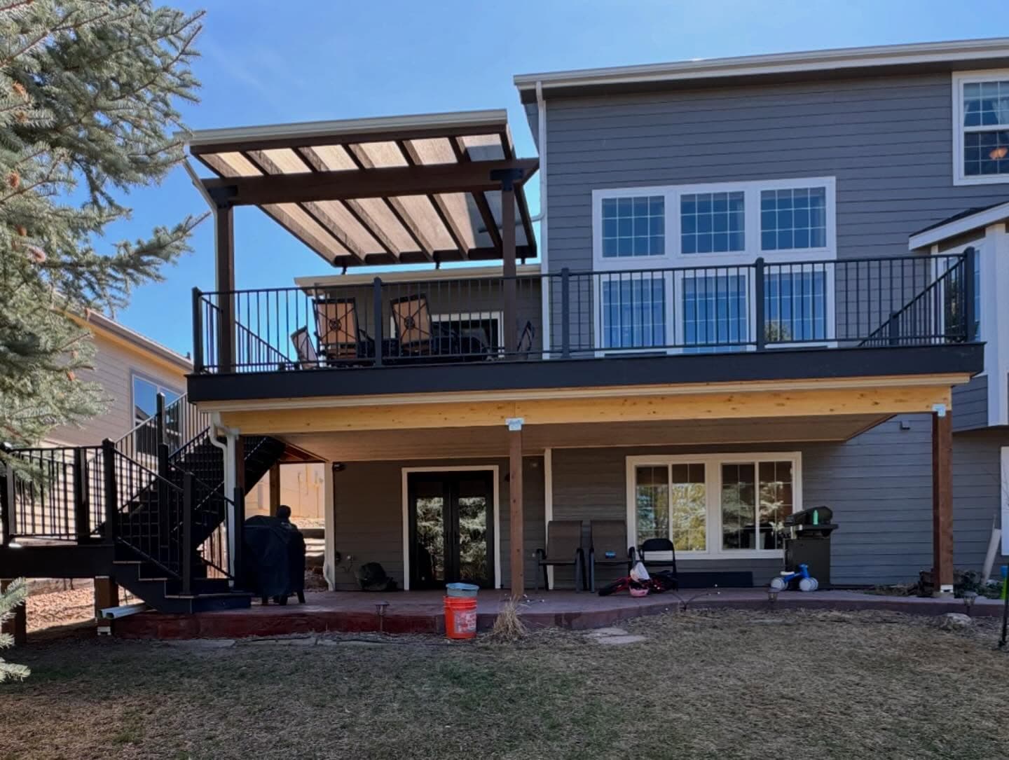 Upper deck with a louvered pergola and black railing above a covered patio with a tongue-and-groove ceiling