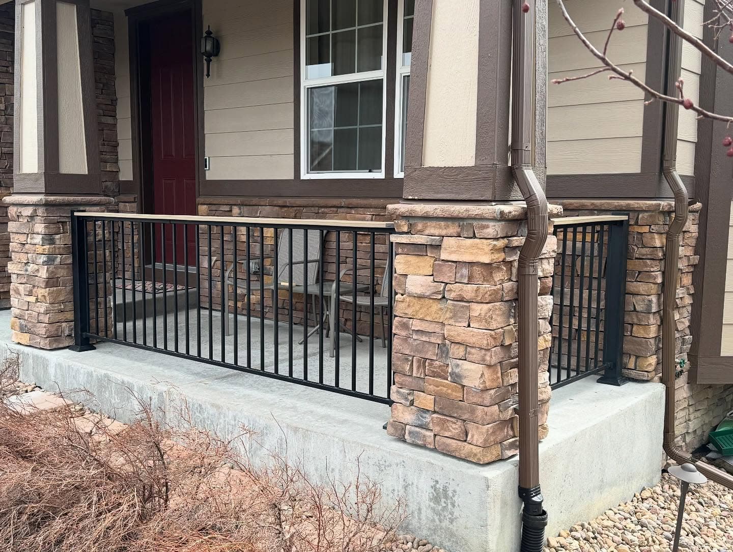 Black aluminum railing with a composite top cap installed on a stone-columned concrete front porch