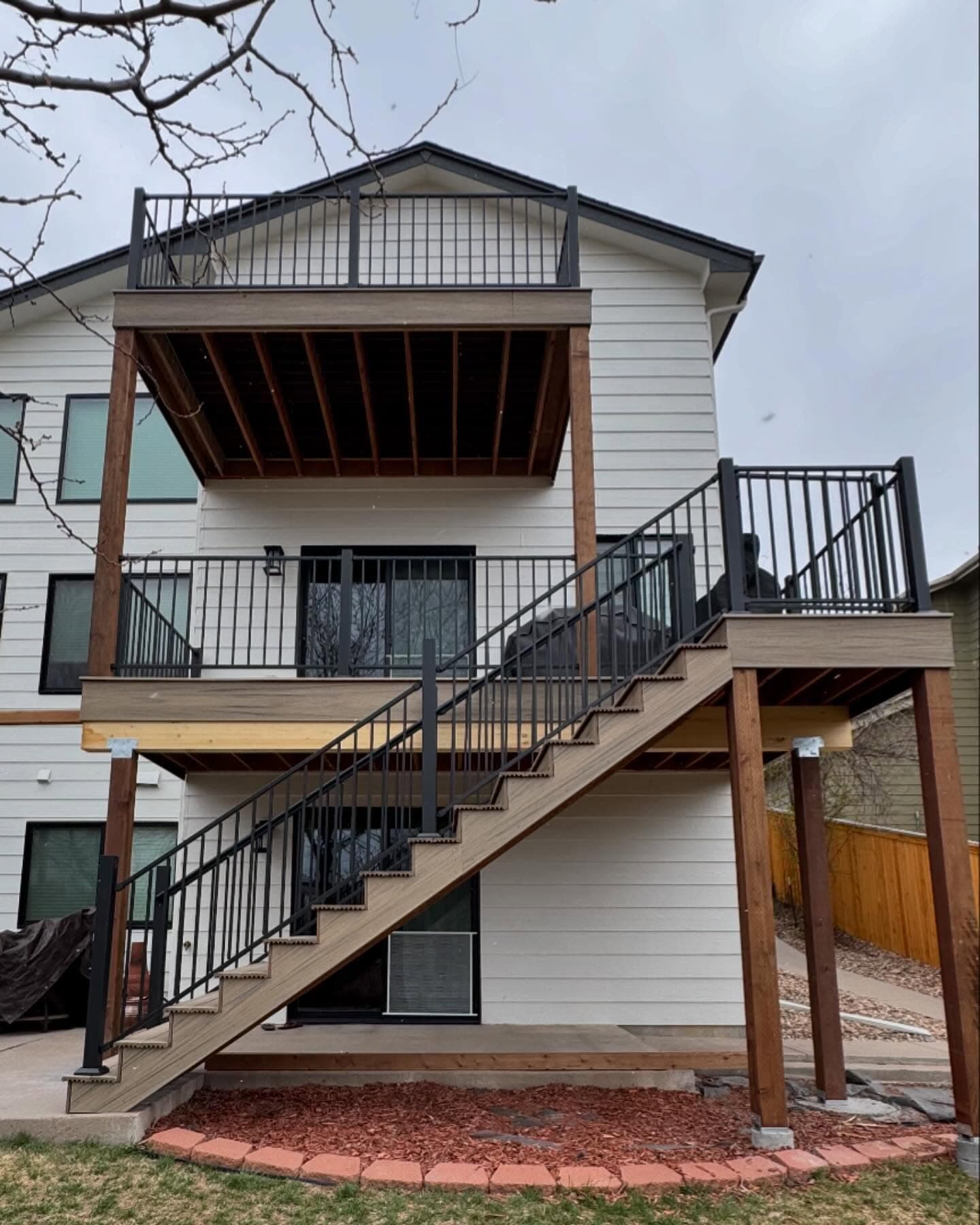 Three-story composite deck and stair run with black railing on a white two-story home