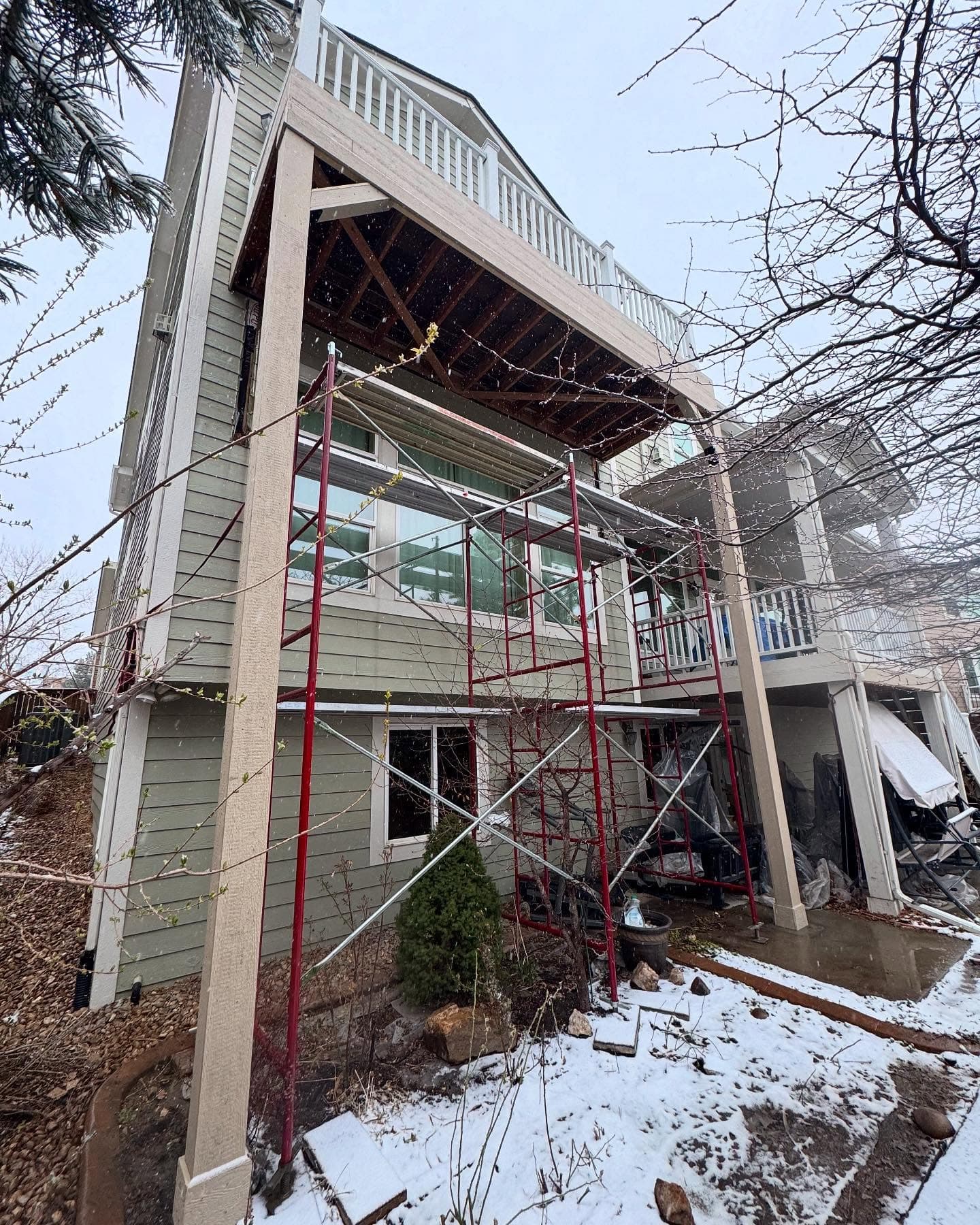 Scaffolding set up under a three-story deck mid-rebuild on a snowy day