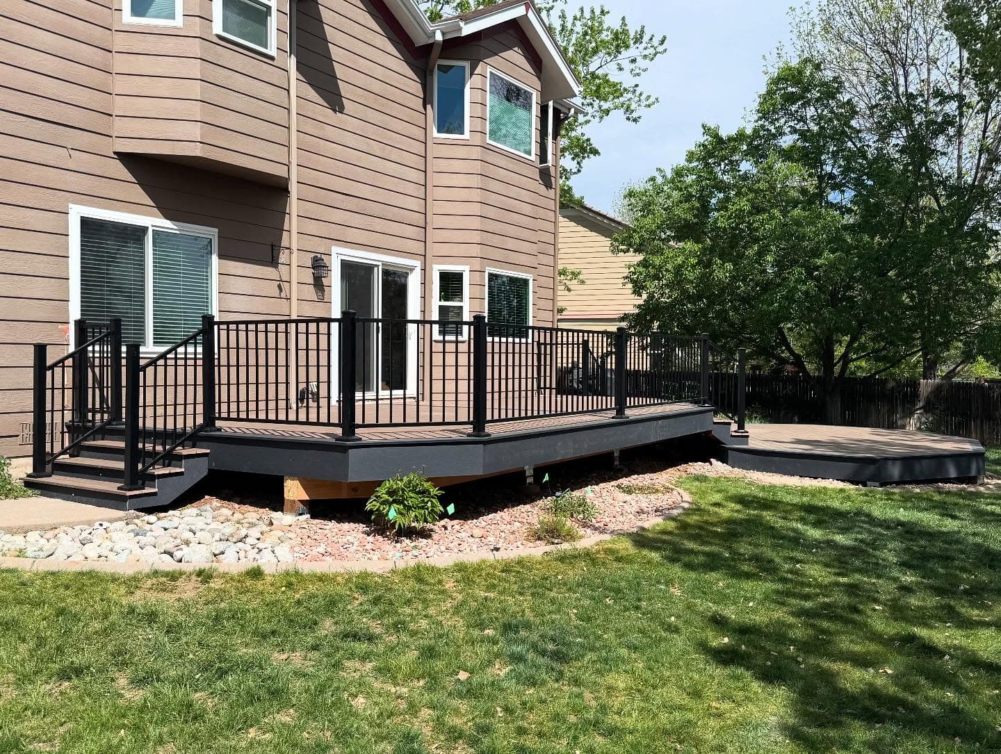 Angled ground-level composite deck with black railing and a separate landing pad on a green lawn