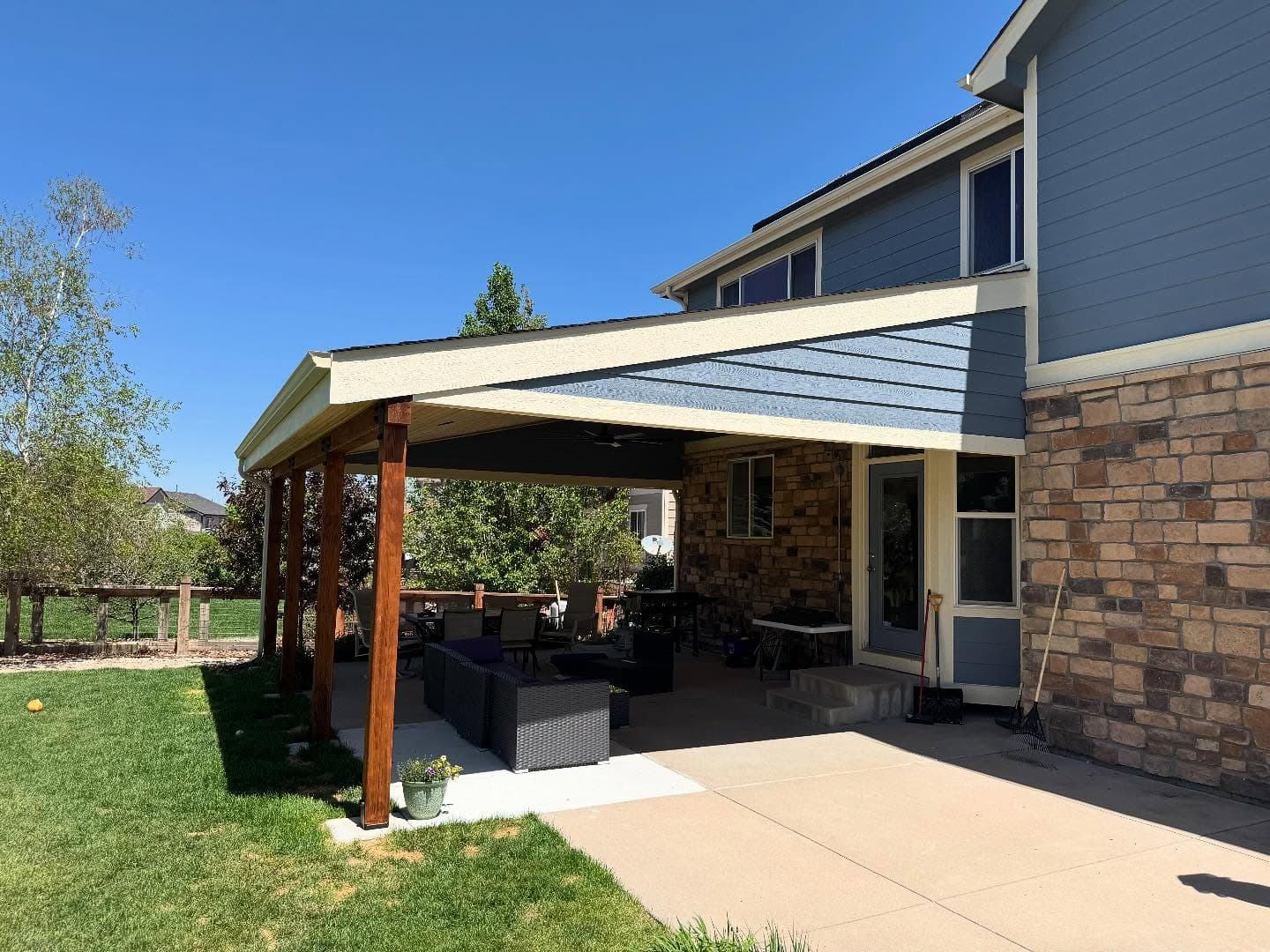 Attached patio cover with a metal roof and stained timber posts shading a concrete patio