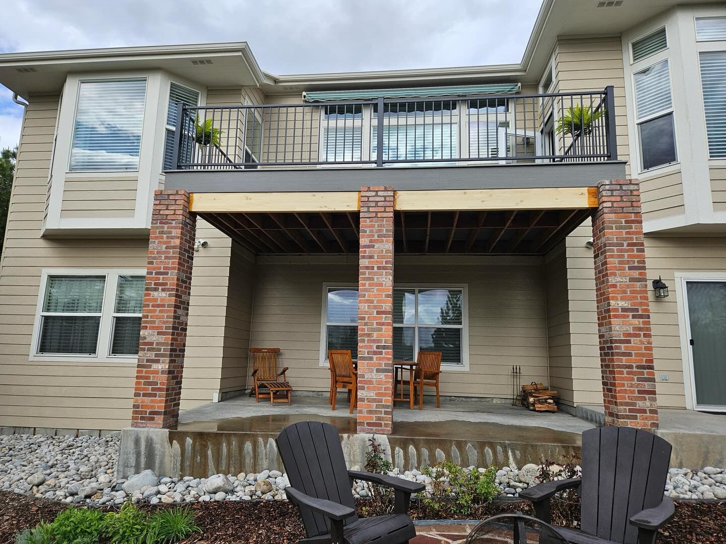 Second-story deck with black railing carried on brick columns above a covered patio