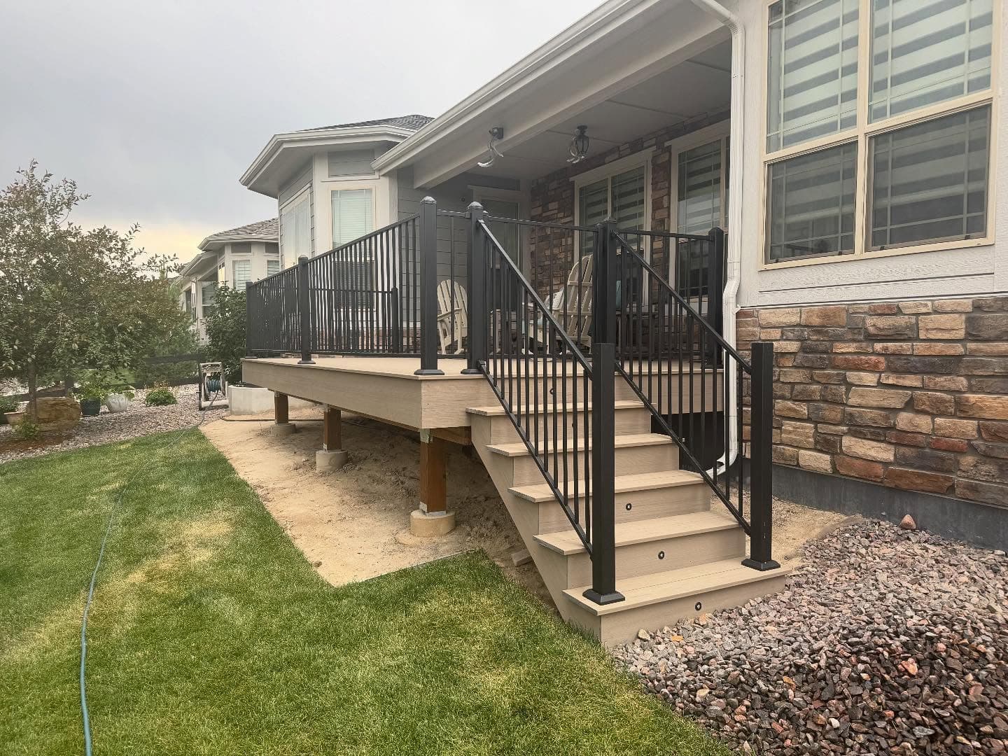 Low composite deck with black aluminum railing and wide stairs beside a stone-front home