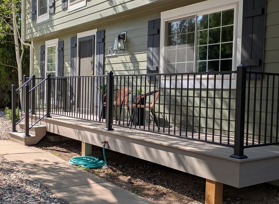 Composite deck with black metal railing overlooking open prairie, furnished with a fire table and Adirondack chairs