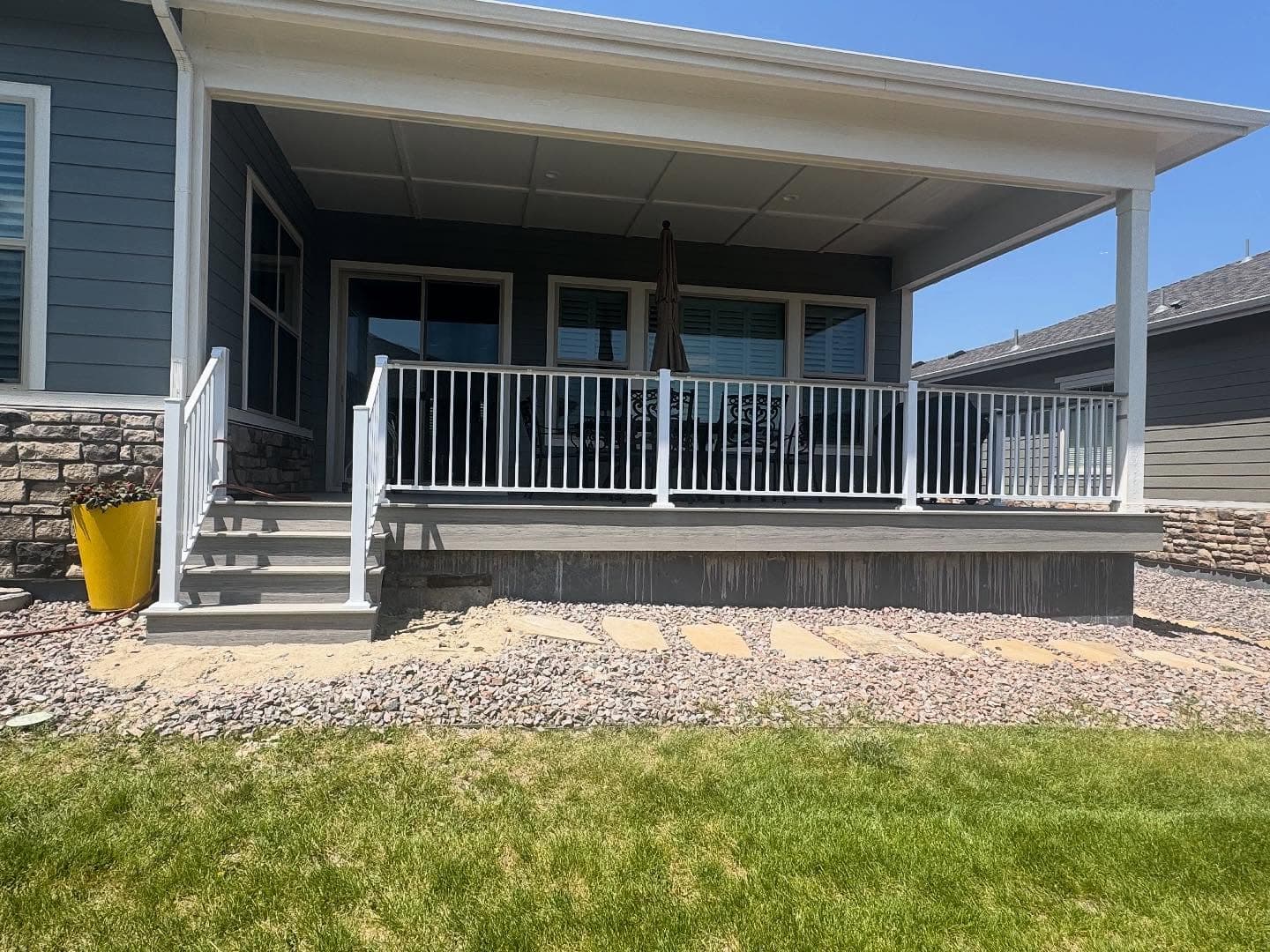 Covered front porch with gray composite decking and white railing on a blue home