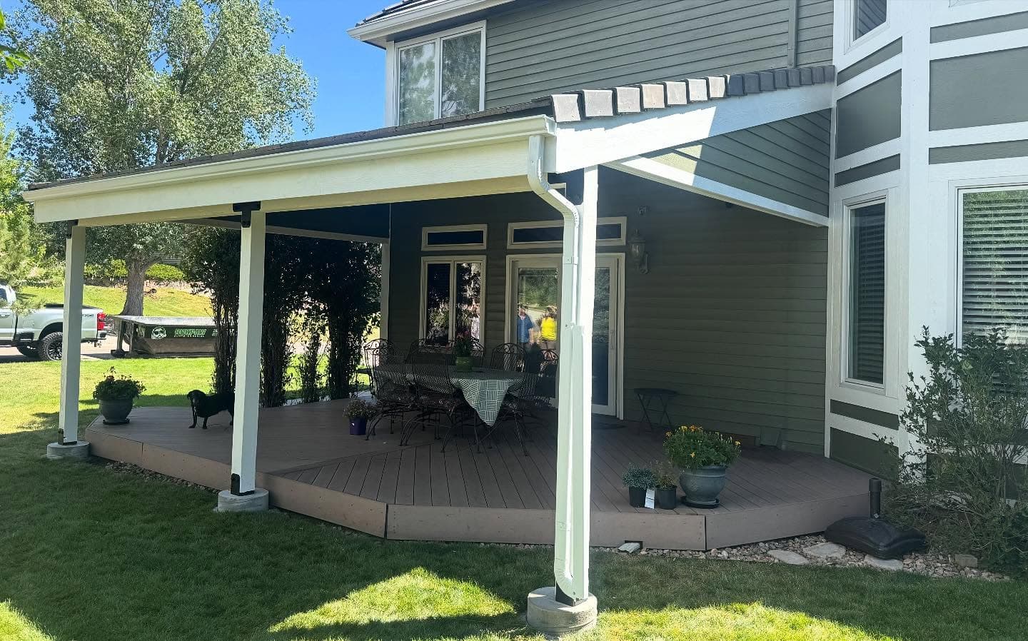 Wraparound composite deck under a white patio cover with timber posts and a dining set