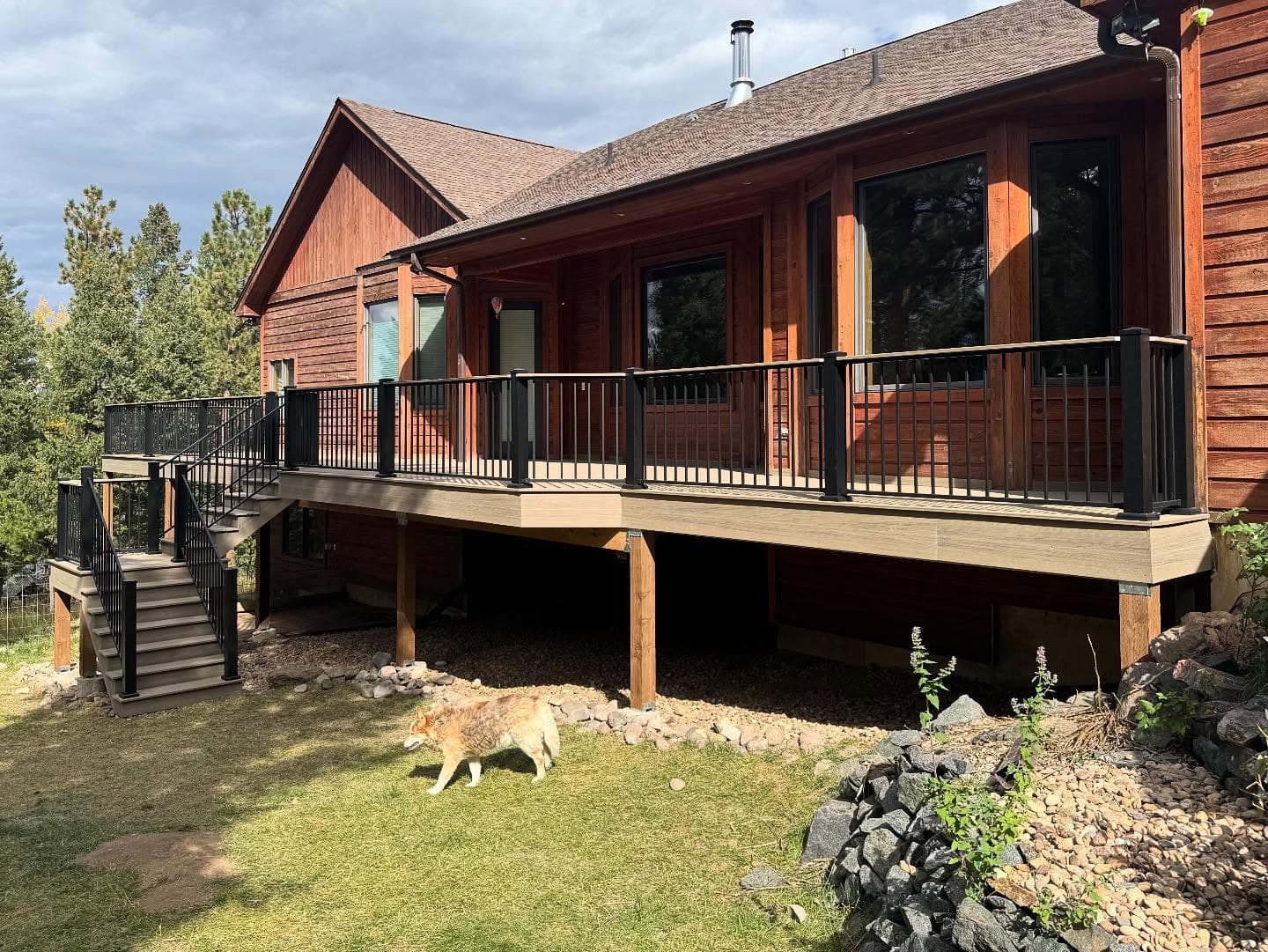 Long composite deck with black railing wrapping a cedar-sided mountain home in the pines