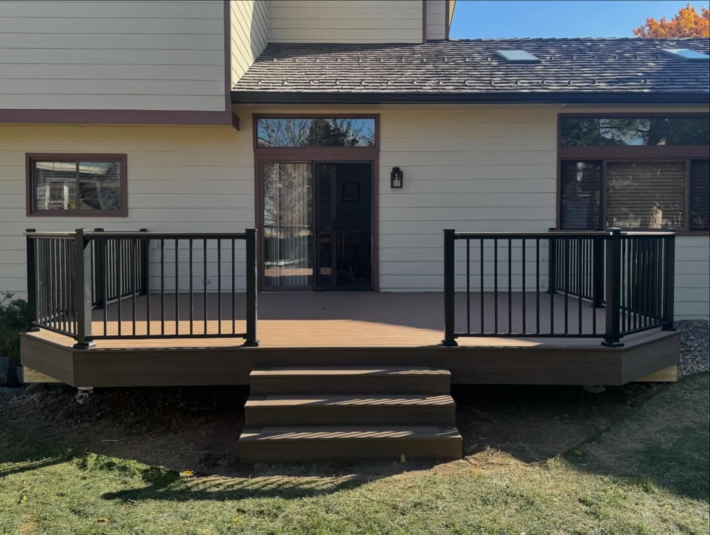 Composite deck with black aluminum railing and steps off the back of a cream-sided home