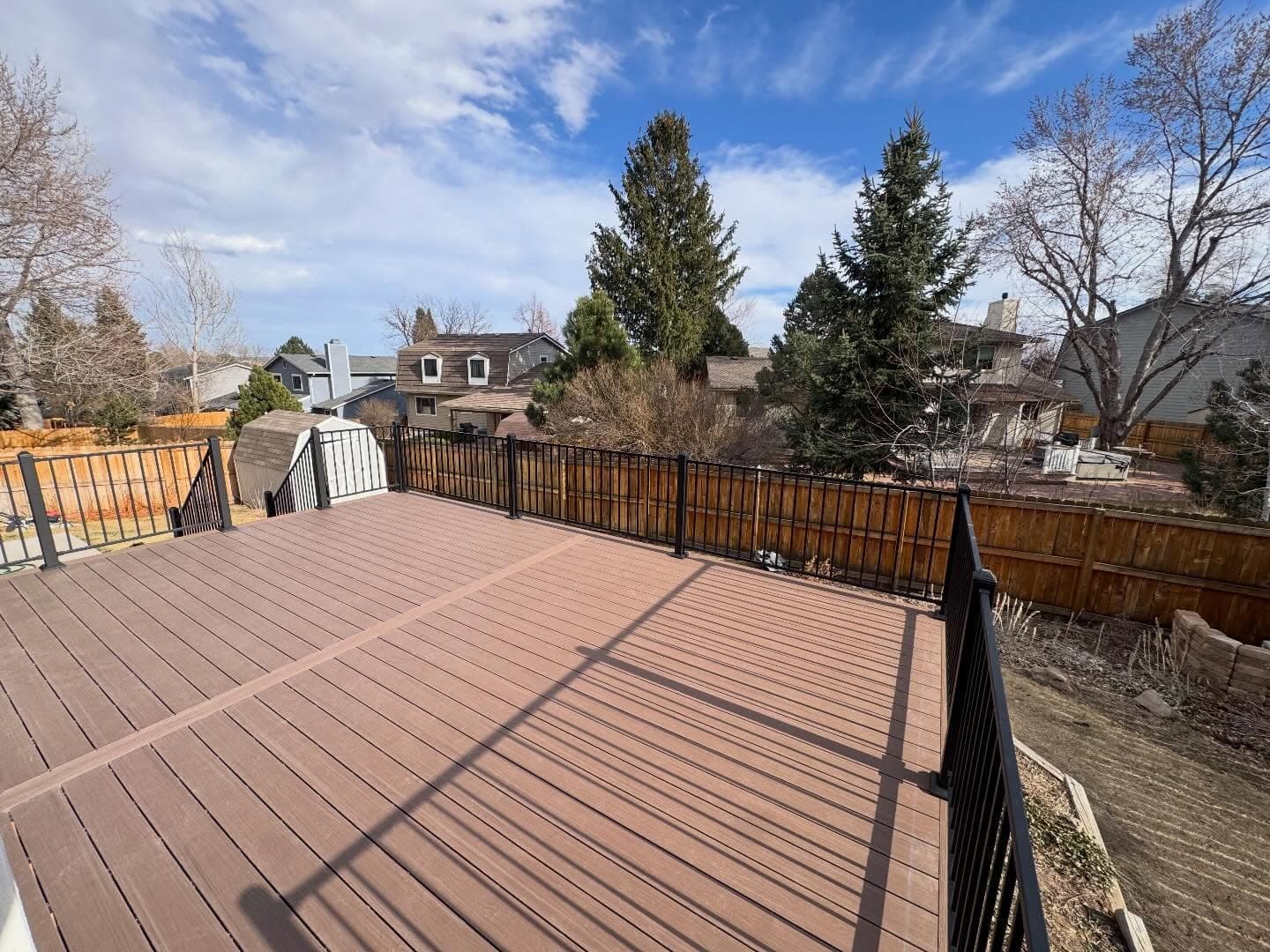 Wide brown composite deck surface with black aluminum railing looking out over a fenced backyard