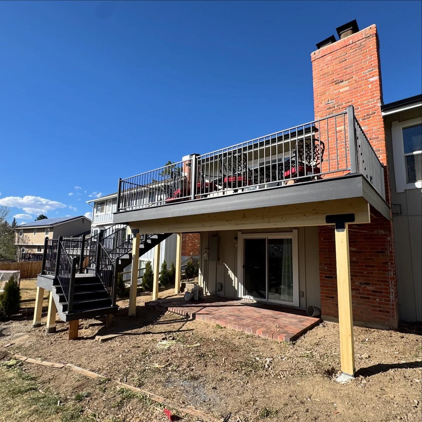 Elevated deck with black railing and stairs on a brick home, framing complete over a lower patio